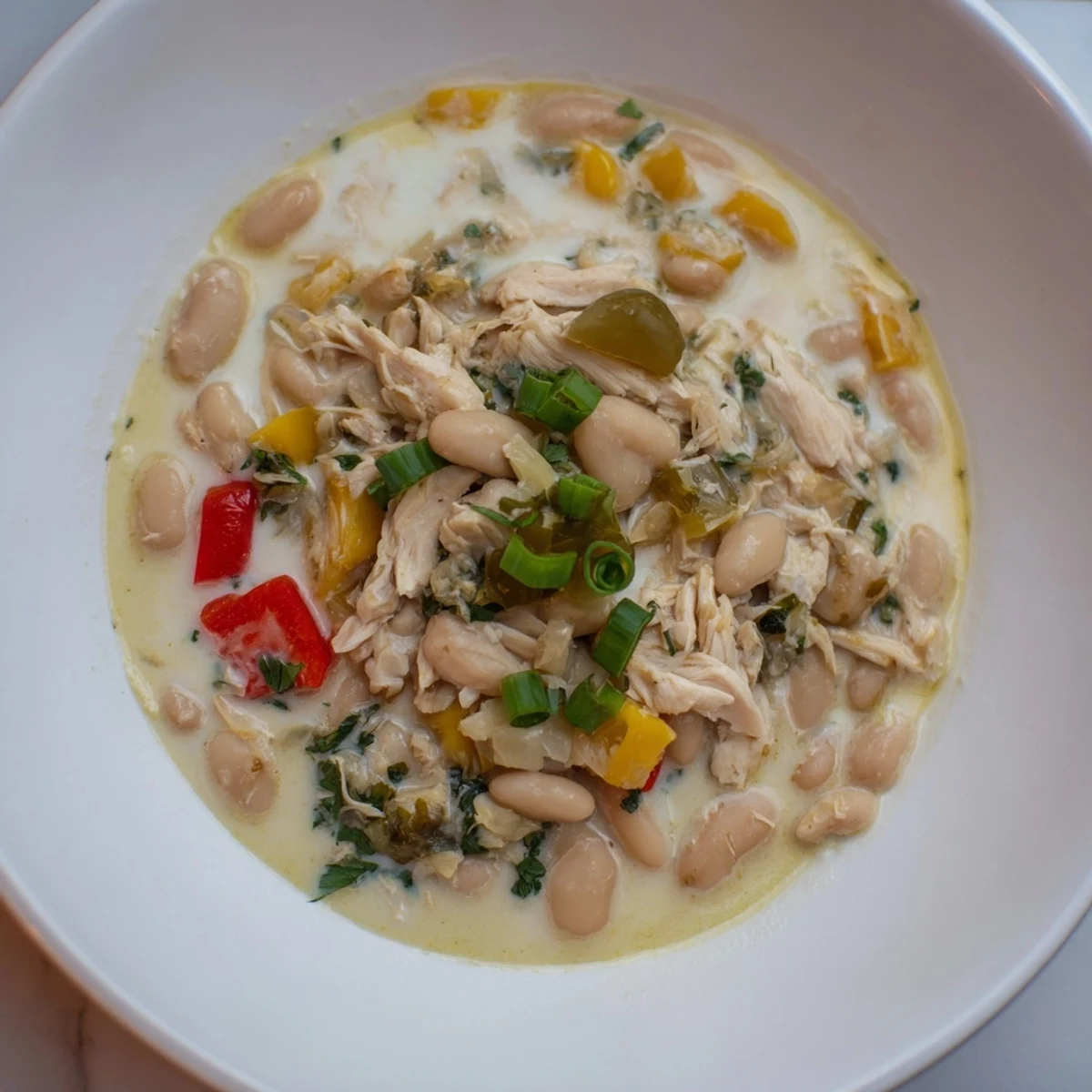 Close-up of a bubbling creamy white chicken chili with visible beans and tender chicken.