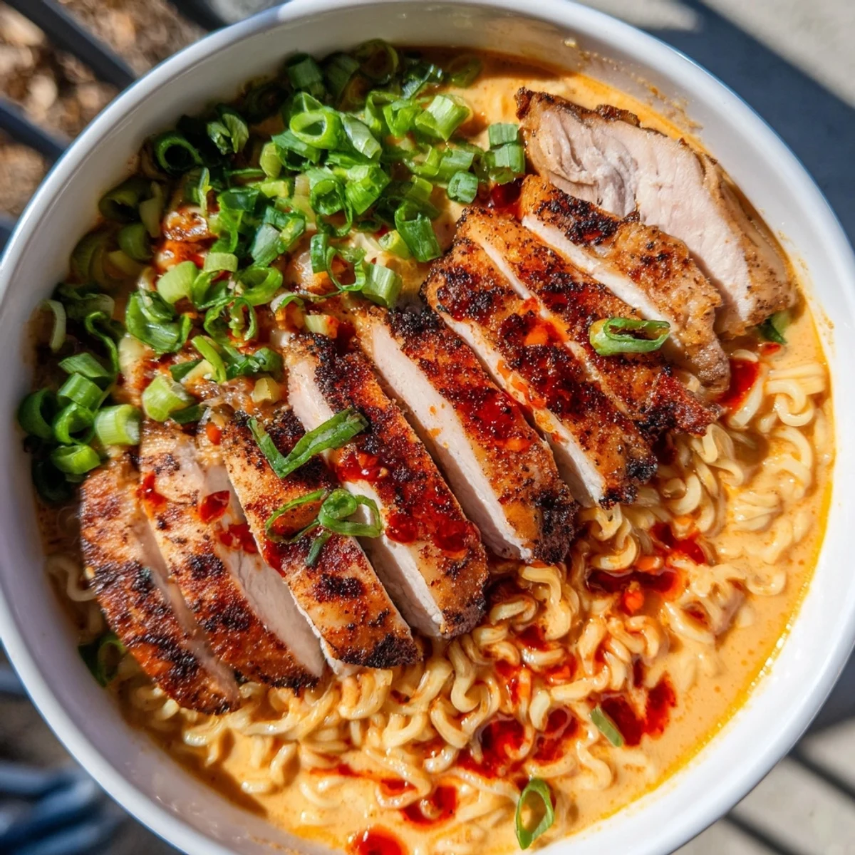 Steaming bowl of Fiery Chicken Ramen, showcasing tender chicken, rich broth, and fresh green onion garnish.