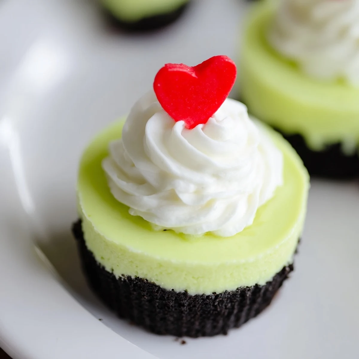 Miniature Grinch Cheesecakes, with a vibrant green hue, look creamy and perfect with red heart sprinkles.