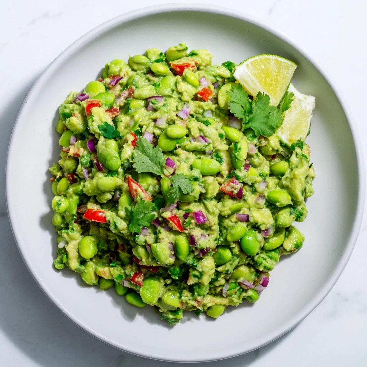 Close-up of fresh Edamame Guacamole, showcasing chunks of tomato and vibrant cilantro, ideal as a snack.