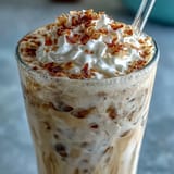 A frothy Vanilla Bean Coconut Frappuccino Mocktail topped with whipped coconut cream and toasted coconut flakes.