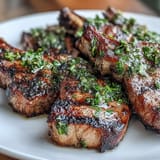 Grilled lamb chops topped with vibrant mint gremolata, garnished with parsley and lemon for a fresh, Mediterranean flavor.