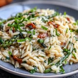 A colorful bowl of spring orzo primavera with fresh asparagus, peas, and zucchini tossed in parmesan and basil.