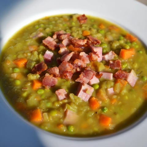Steaming bowl of Split Pea Soup with canned ham, garnished with crispy bacon, ready to serve.