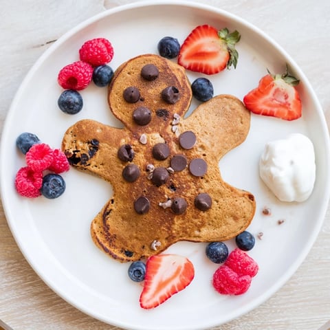 Fluffy gingerbread boy pancakes surrounded by colorful berries and creamy yogurt; a festive breakfast.