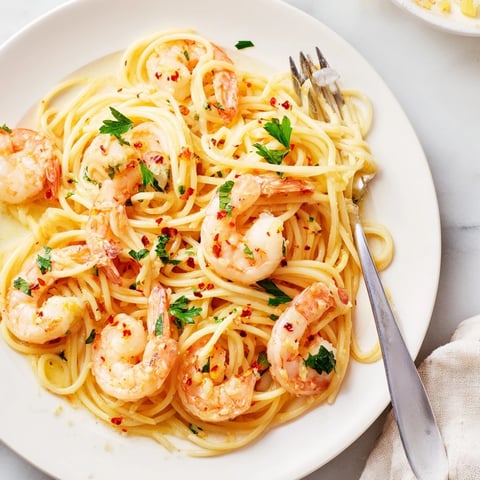 Plump, pink shrimp coated in a glossy lemon garlic butter sauce, served over al dente spaghetti on a white plate.
