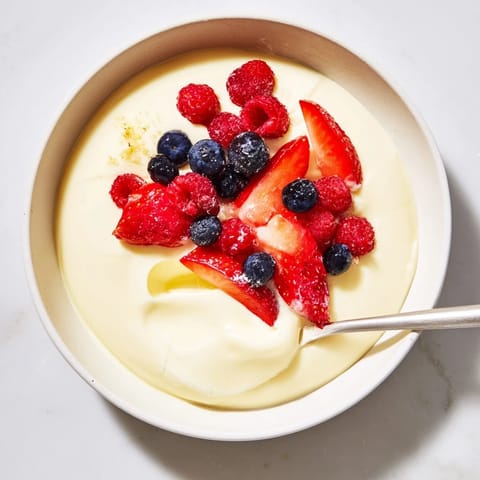 Chilled silky vanilla pudding garnished with vibrant, juicy berries for a refreshing treat.  