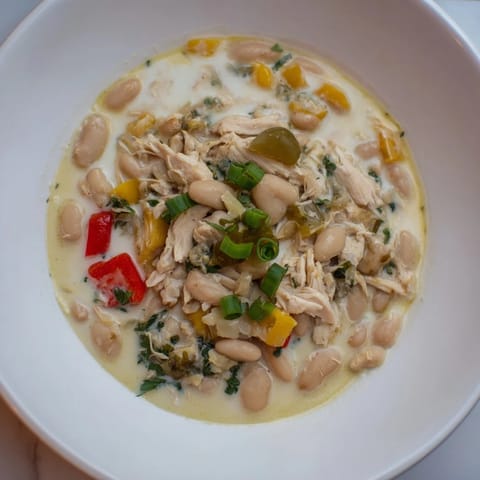 Close-up of a bubbling creamy white chicken chili with visible beans and tender chicken.