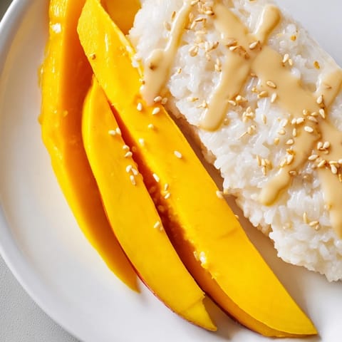 A close-up of glistening Thai Mango Sticky Rice, fragrant with coconut milk and topped with sesame seeds.