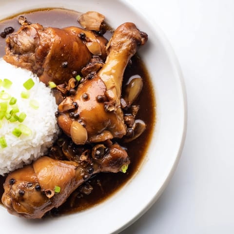 Savory Filipino Chicken Adobo simmering in a skillet, showcasing the rich, dark sauce coating the chicken.