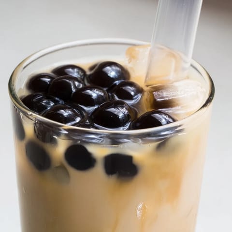 A close-up of a tall glass of Boba Tea Hack, rich brown tea, and sweetened condensed milk swirls.