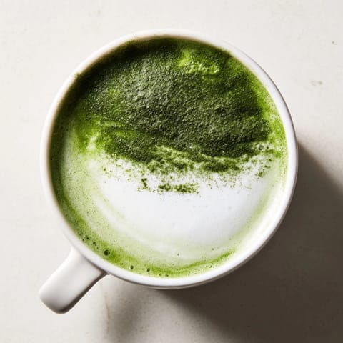 Smooth matcha green tea latte served in a cozy café setting, the steamed milk swirling gently with a sprinkle of matcha powder on the frothy top.  