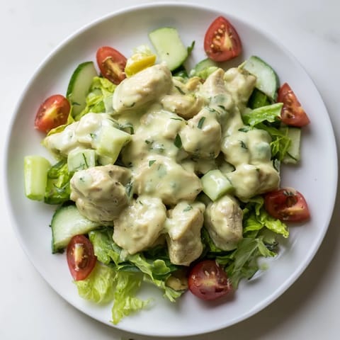 Fresh avocado ranch chicken salad garnished with herbs, paired with cherry tomatoes and cucumbers on a rustic plate.