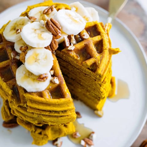 A close-up view of golden Anti-Inflammatory Adaptogenic Turmeric Waffles topped with creamy Greek yogurt and sliced bananas. 