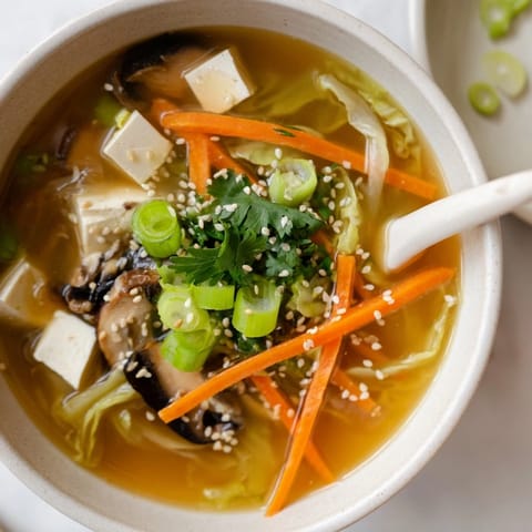 A warm bowl of Ginger-Miso Winter Soup, garnished with toasted sesame seeds and fresh scallions, steaming gently.