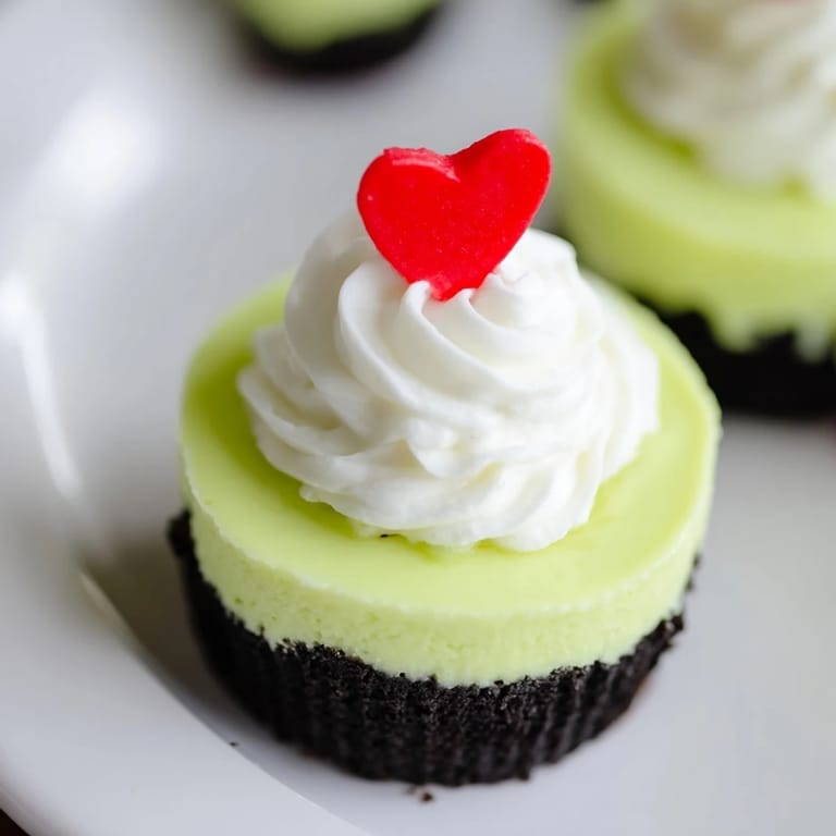 Miniature Grinch Cheesecakes, with a vibrant green hue, look creamy and perfect with red heart sprinkles.