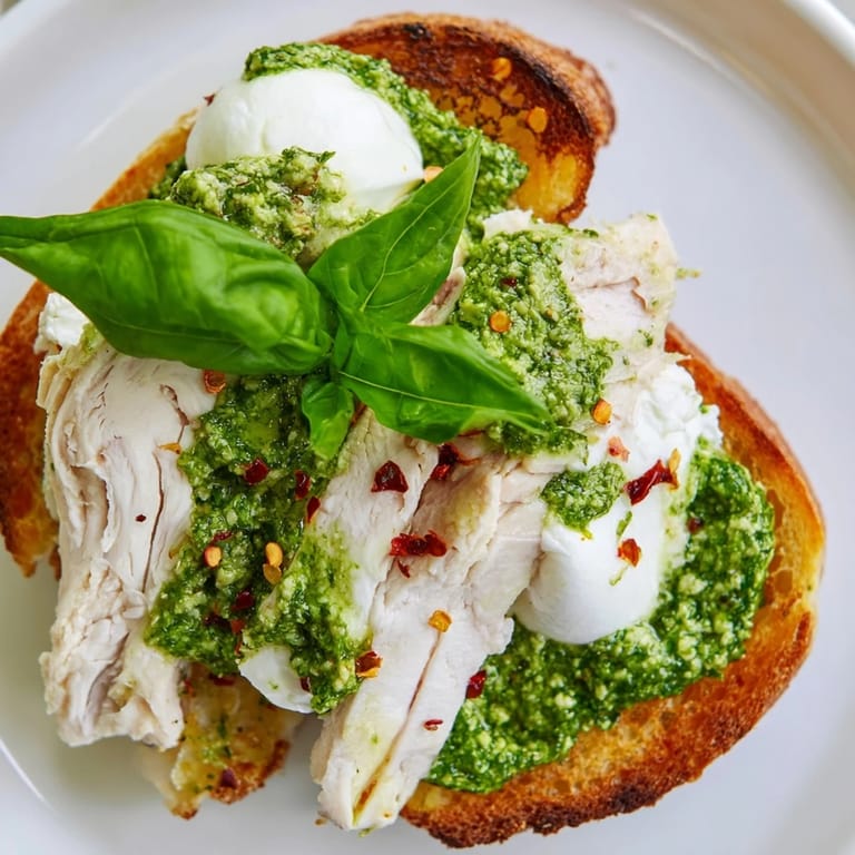 Pesto chicken burrata toast served on a rustic wooden board, featuring golden-brown bread, juicy chicken, and melting burrata for a perfect Italian-inspired bite.  