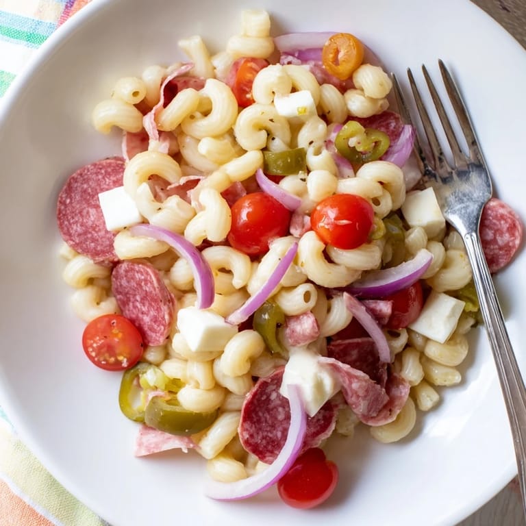 Ready for a spring gathering, the Spring Antipasto Pasta Salad is plated in a white bowl, garnished with fresh herbs and chili flakes.
